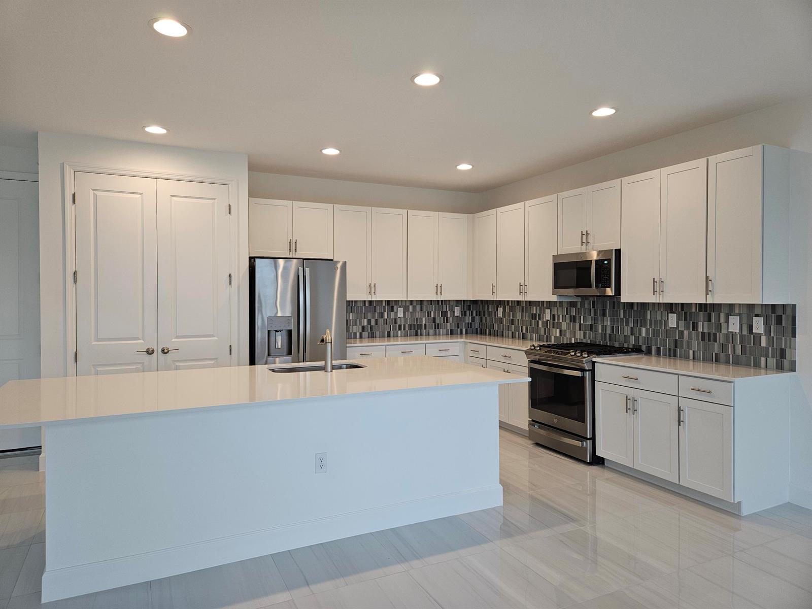 A modern kitchen features white cabinetry, stainless steel appliances, a center island, and tiled backsplash — 17199 Tawny Owl Trail, FL 33470, FL