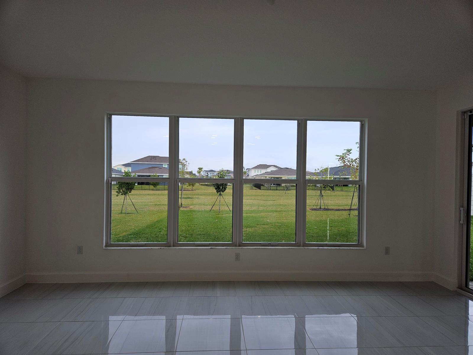 A bright, empty room with large windows overlooking a grassy backyard and neighboring houses — 17199 Tawny Owl Trail, FL 33470, FL