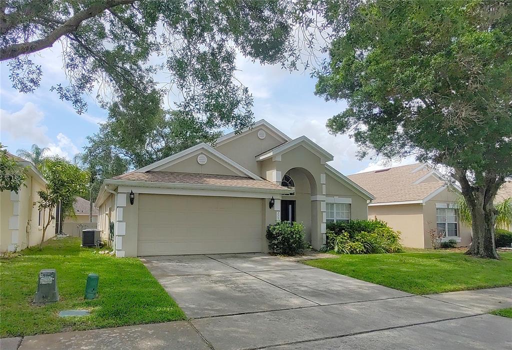 A single-story suburban house with a beige stucco exterior, a two-car garage, and a driveway — 2741 BELLEWATER PLACE, OVIEDO, FL