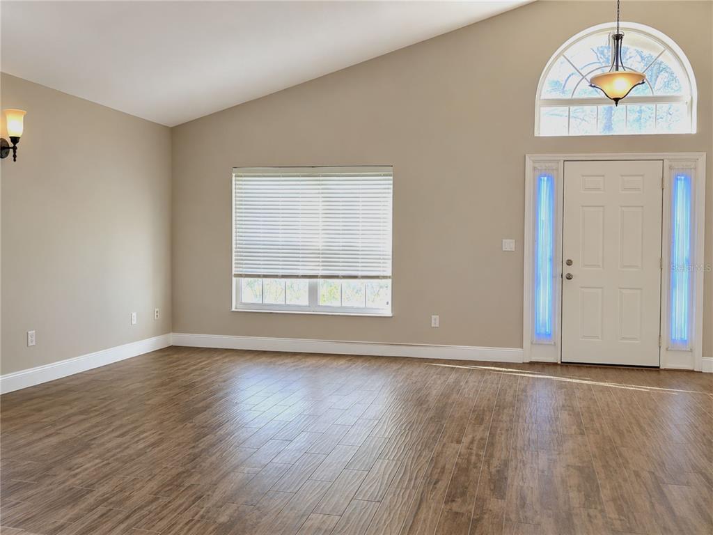 An empty room with wood-look tile flooring, a vaulted ceiling, and a front door — 2741 BELLEWATER PLACE, OVIEDO, FL