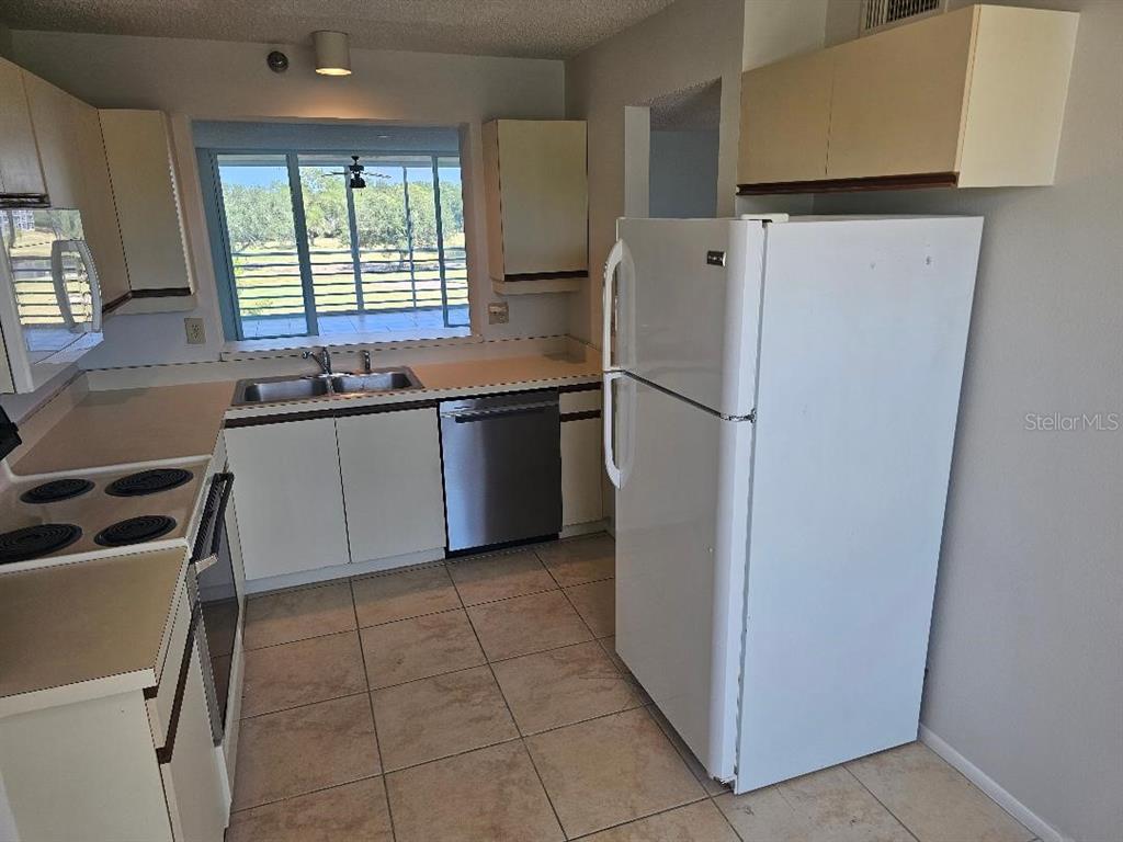 A kitchen with white cabinets, stainless steel appliances, and tile flooring overlooks a screened porch — 4410 FAIRWAYS BOULEVARD UNIT 206, BRADENTON, FL