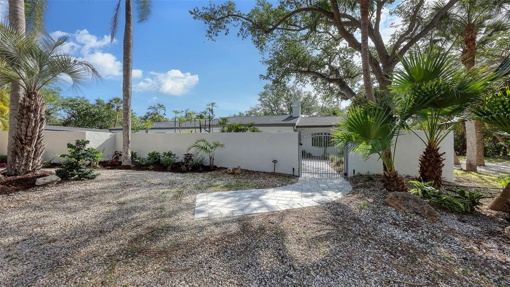 A white wall and gate enclose a house entrance with a stone walkway and landscaping — 7345 PINE NEEDLE ROAD, SARASOTA, FL