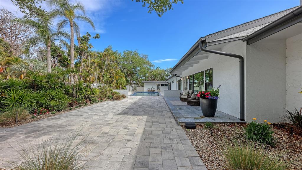A paved patio leads to a swimming pool alongside a white house with palm trees — 7345 PINE NEEDLE ROAD, SARASOTA, FL
