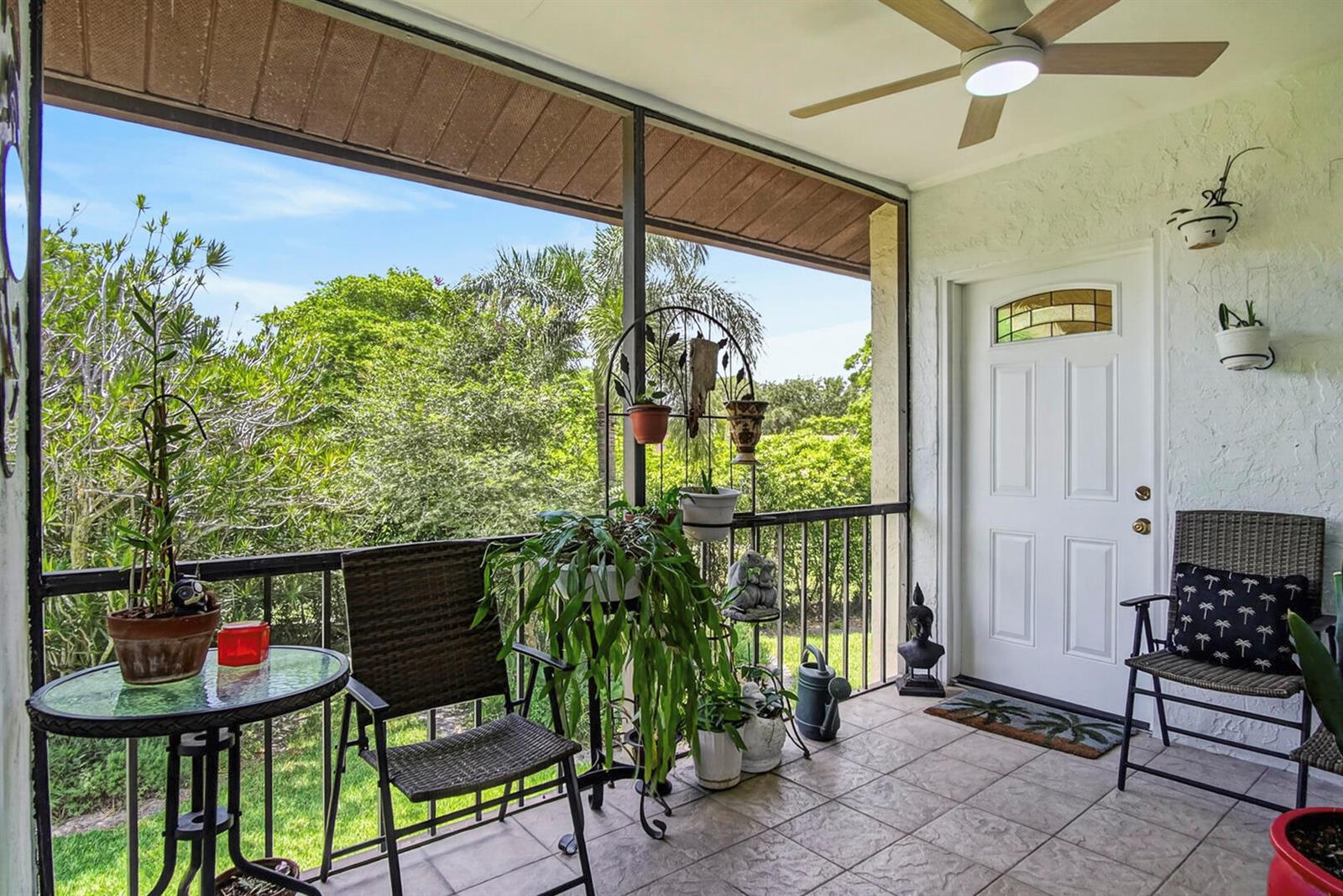A screened-in porch features tiled flooring, wicker chairs, potted plants, and a ceiling fan — 5930 Whispering Pine Way # 2, FL 33463, FL
