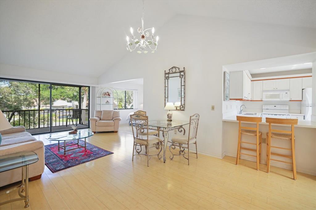 A bright open-concept living and dining area with light wood flooring and a vaulted ceiling — 715 BIRD BAY CIRCLE UNIT 120, VENICE, FL