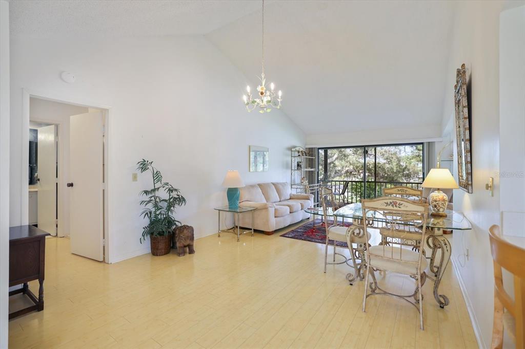 A living and dining area with light wood floors, vaulted ceilings, and a glass-topped table — 715 BIRD BAY CIRCLE UNIT 120, VENICE, FL