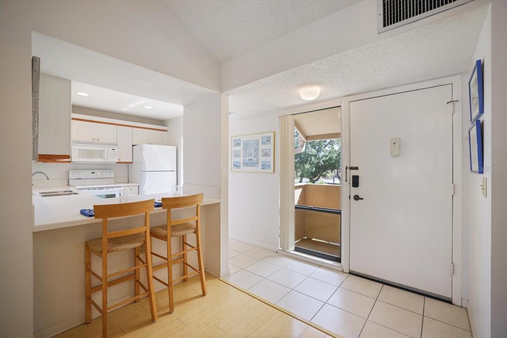 A kitchen with a breakfast bar, white appliances, and a door leading to a balcony — 715 BIRD BAY CIRCLE UNIT 120, VENICE, FL