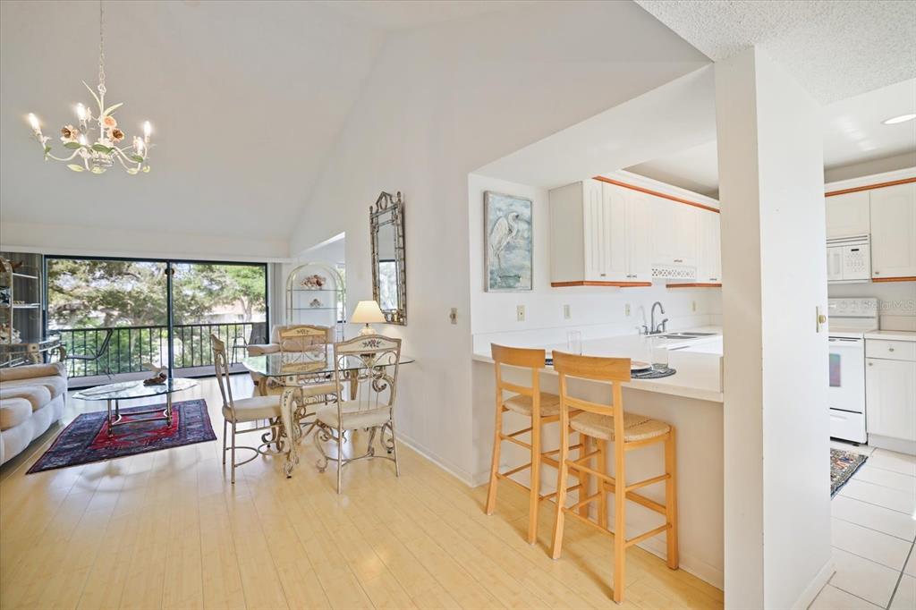 An open-concept living and dining area features light wood flooring, a breakfast bar, and balcony — 715 BIRD BAY CIRCLE UNIT 120, VENICE, FL