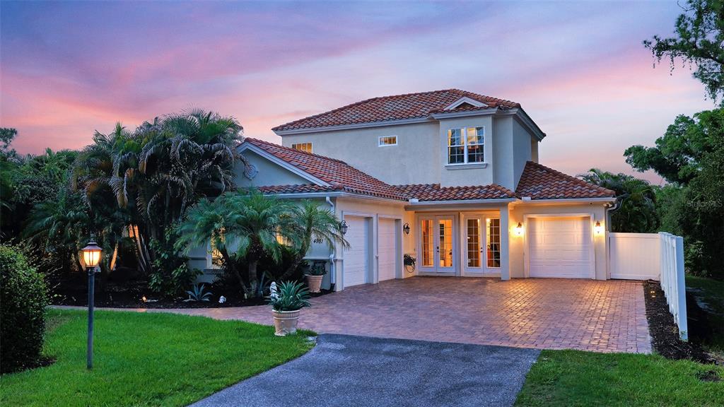 A two-story house with a tiled roof, brick driveway, and attached garages at dusk — 4981 HUBNER CIRCLE, SARASOTA, FL