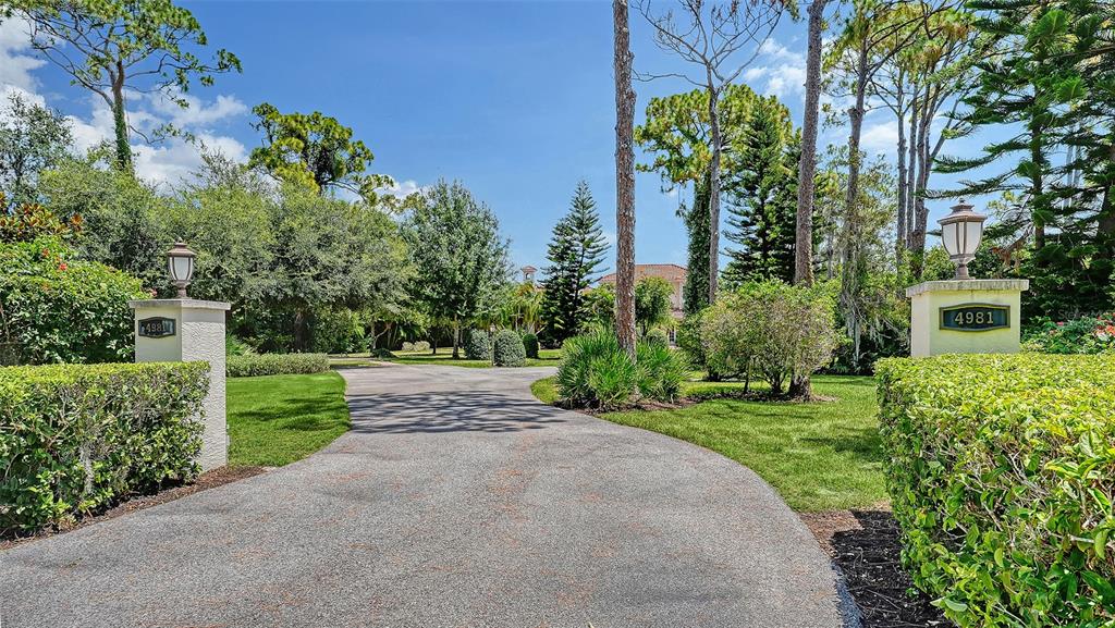 A paved driveway leads toward a house through a landscaped yard with two stone pillars — 4981 HUBNER CIRCLE, SARASOTA, FL