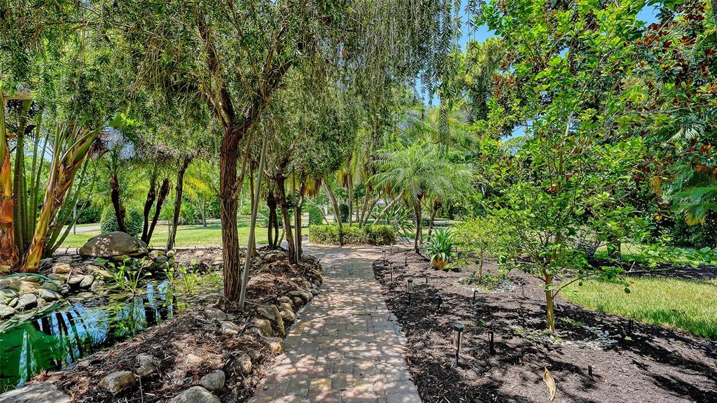 A brick path leads through a lush garden with a small pond and various trees — 4981 HUBNER CIRCLE, SARASOTA, FL