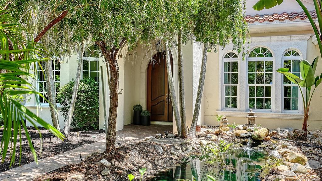 The exterior of a house features a wooden arched front door, arched windows, and a pond — 4981 HUBNER CIRCLE, SARASOTA, FL