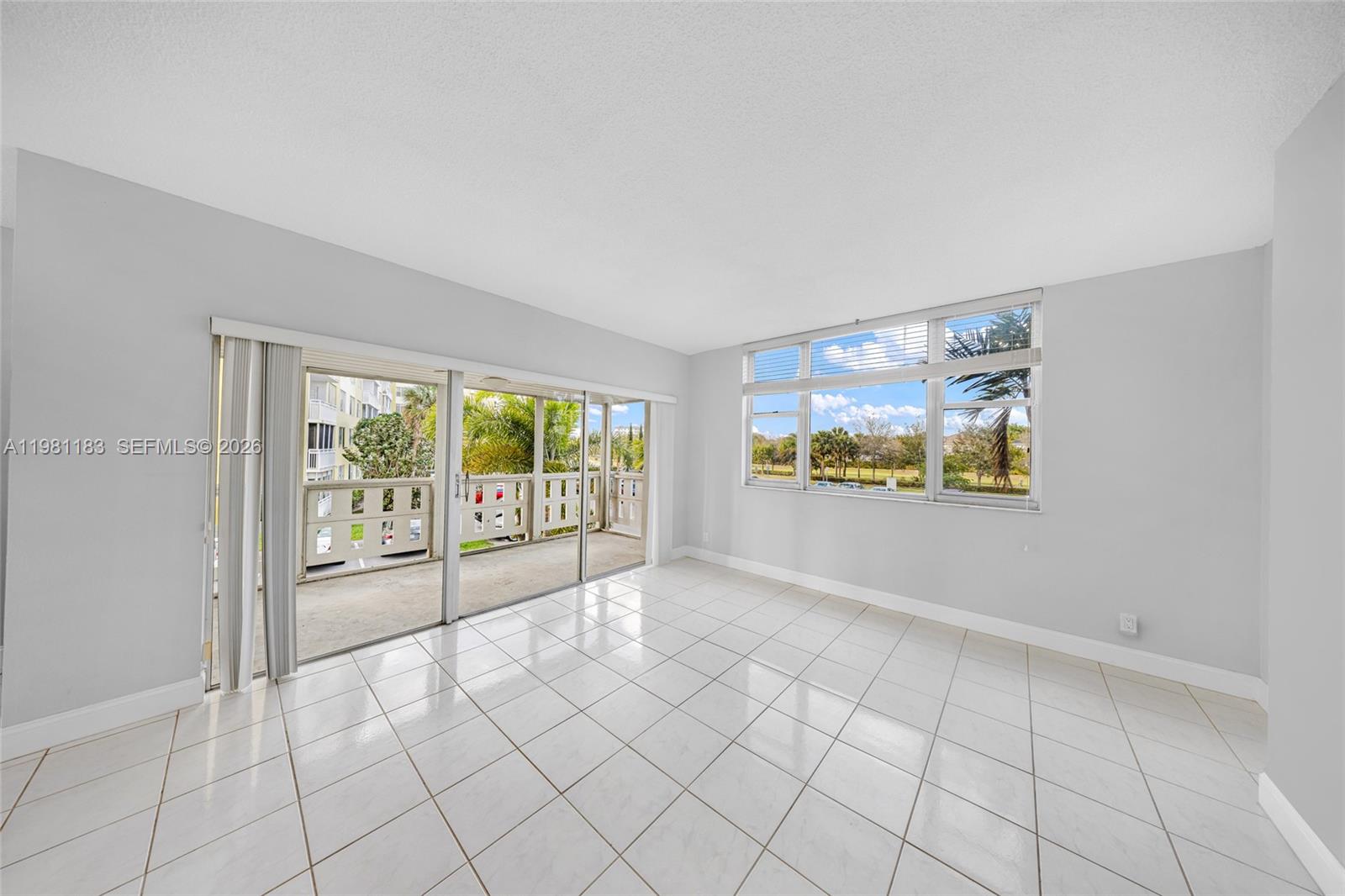 A bright, empty room features white tile flooring, sliding glass doors to a balcony, and windows — 4350 Hillcrest Dr # 200, Hollywood FL 33021, HOLLYWOOD, FL