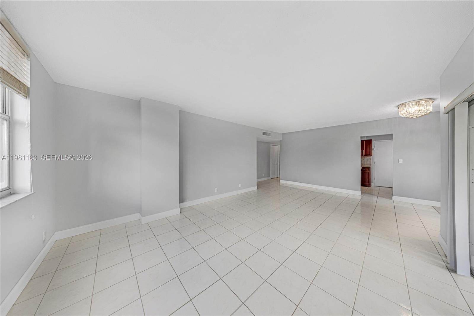 A spacious, empty living room features light gray walls, white tile flooring, and a chandelier — 4350 Hillcrest Dr # 200, Hollywood FL 33021, HOLLYWOOD, FL