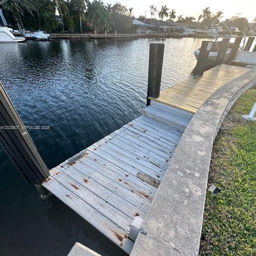 A wooden boat dock extends over a canal next to a concrete seawall — HALLANDALE BEACH, FL
