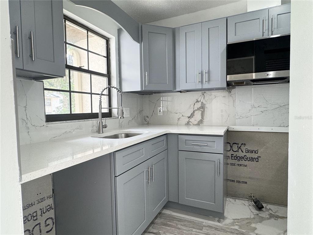 A kitchen features grey cabinets, white marble-look countertops, and unfinished wall sections near the floor — 2207 KARL STREET UNIT A, LEESBURG, FL