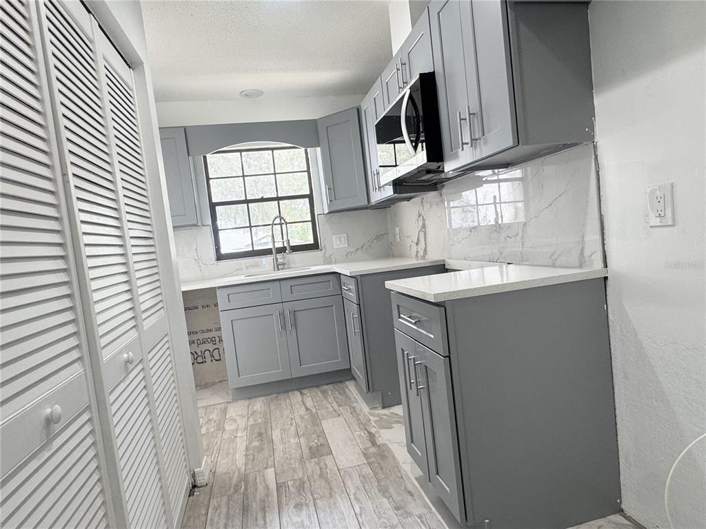 A kitchen features gray cabinets, white countertops, a marble backsplash, and wood-look tile flooring — 2207 KARL STREET UNIT A, LEESBURG, FL