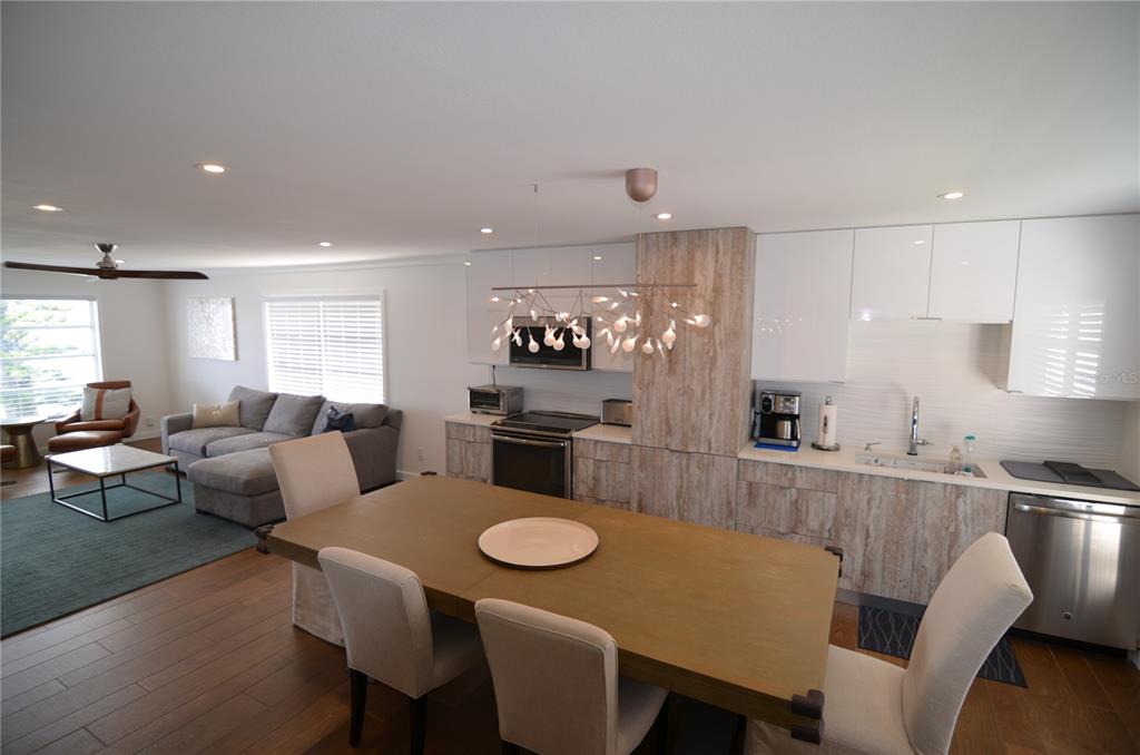 An open-concept kitchen and dining area features wood-look cabinetry, white upper cabinets, and modern lighting — 4420 EXETER DRIVE UNIT 208, LONGBOAT KEY, FL