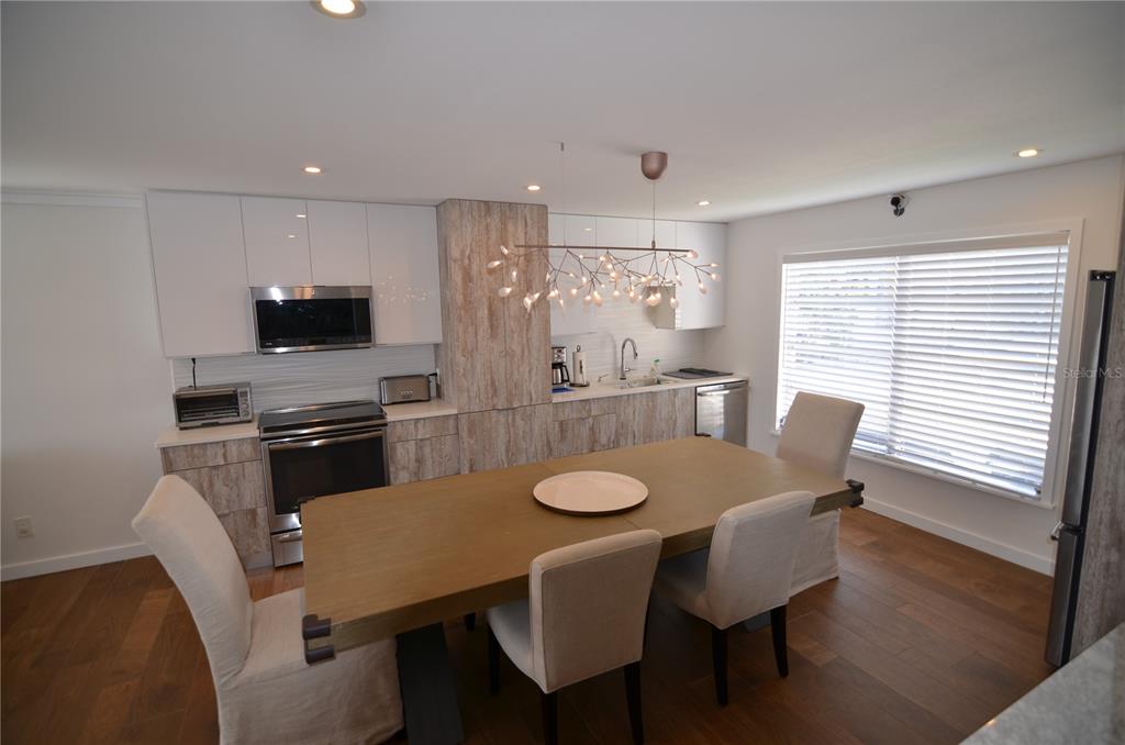 A kitchen with wood-look cabinetry, white upper cabinets, a dining table, and a modern chandelier — 4420 EXETER DRIVE UNIT 208, LONGBOAT KEY, FL