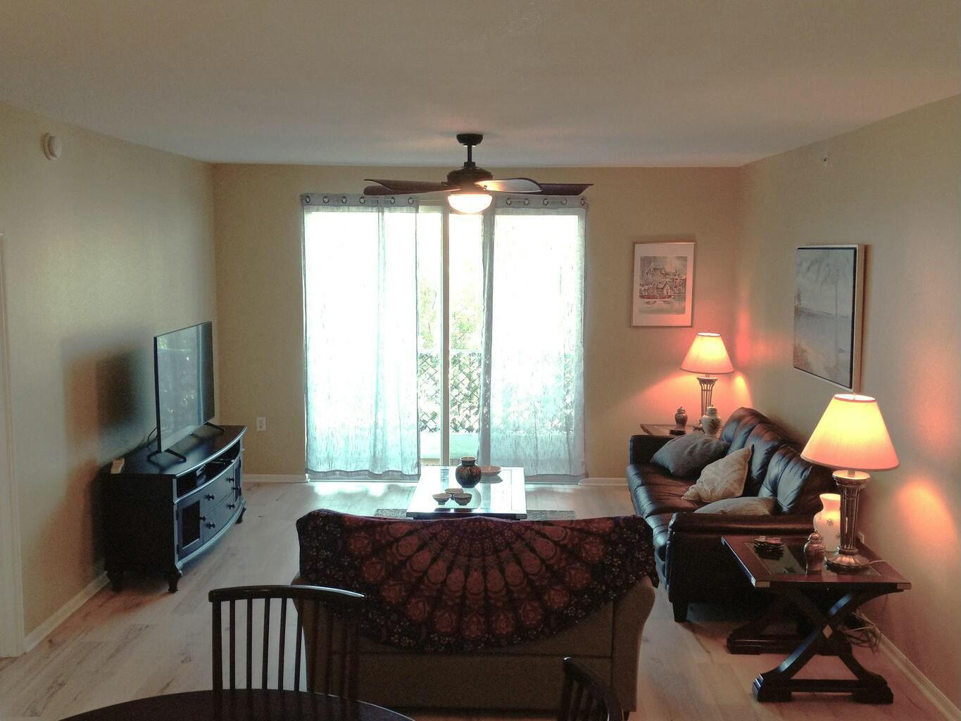 A living room features a dark leather sofa, a television console, and a sliding glass door — 802 W Windward Way # 203, Lantana FL 33462, LANTANA, FL