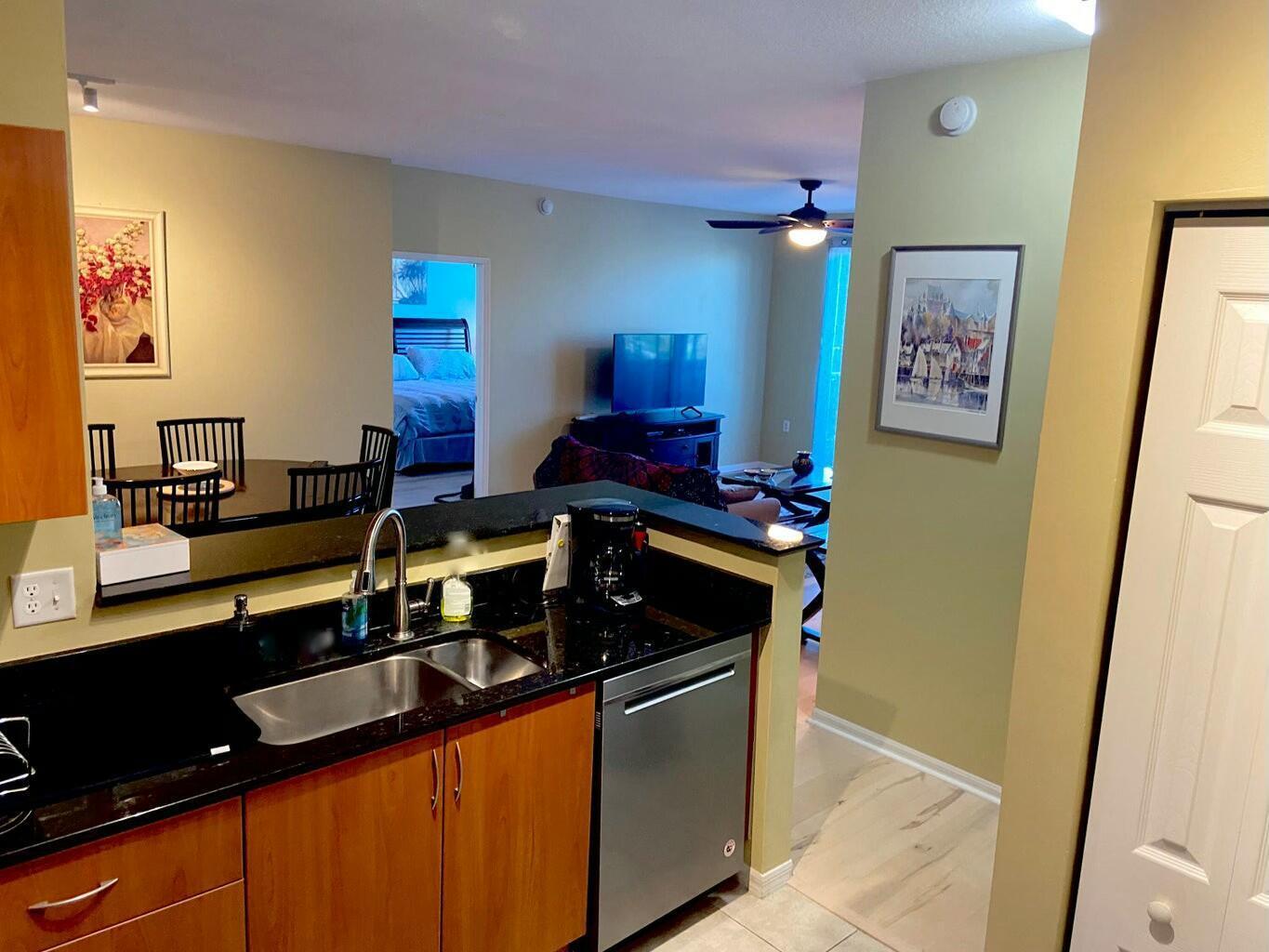 A kitchen with dark countertops and wood cabinets overlooks a living area and dining space — 802 W Windward Way # 203, Lantana FL 33462, LANTANA, FL
