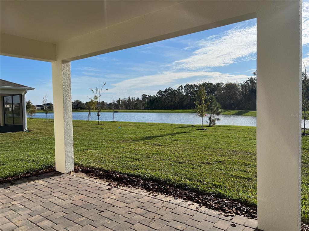 A covered brick patio overlooks a grassy lawn and a pond under a blue sky — 17575 SAW PALMETTO AVENUE, CLERMONT, FL