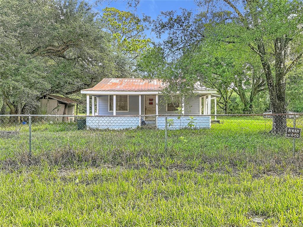 A light blue cottage with a rusted metal roof sits behind a chain-link fence — 1007 HAWTHORN STREET, ZEPHYRHILLS, FL