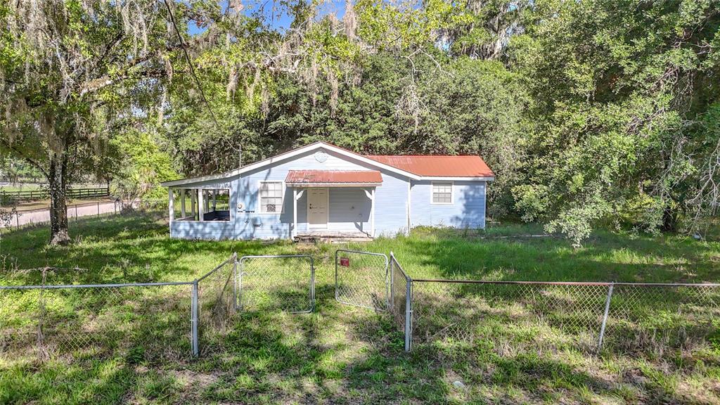 A light blue, single-story house with a red metal roof sits behind a chain-link fence — 1007 HAWTHORN STREET, ZEPHYRHILLS, FL