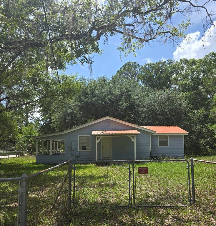 A light blue single-story house with a metal roof sits behind a chain-link fence — 1007 HAWTHORN STREET, ZEPHYRHILLS, FL