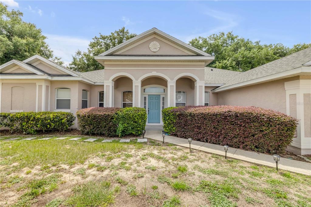 The exterior of a single-story house features a light-colored facade, arched entryway, and landscaping — 36624 GRAND ISLAND OAKS CIRCLE, GRAND ISLAND, FL