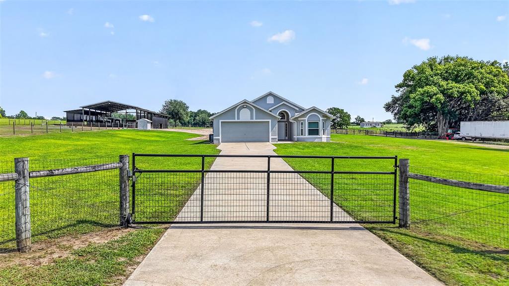 A single-story house with a concrete driveway and metal gate sits on a grassy lot — 14125 SE 175TH STREET, WEIRSDALE, FL