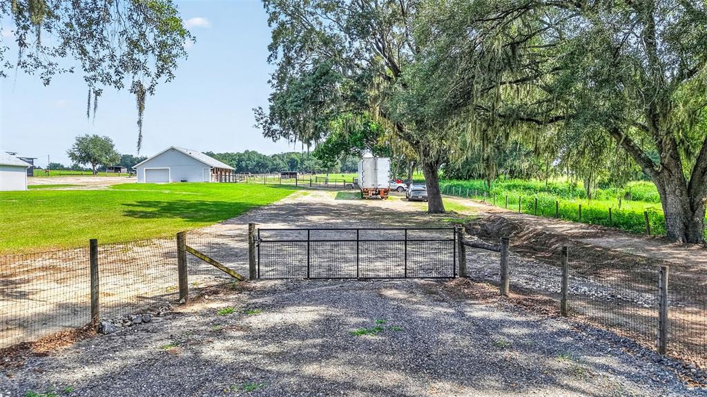 A gravel driveway leads to a metal gate, a large barn, and mature oak trees — 14125 SE 175TH STREET, WEIRSDALE, FL