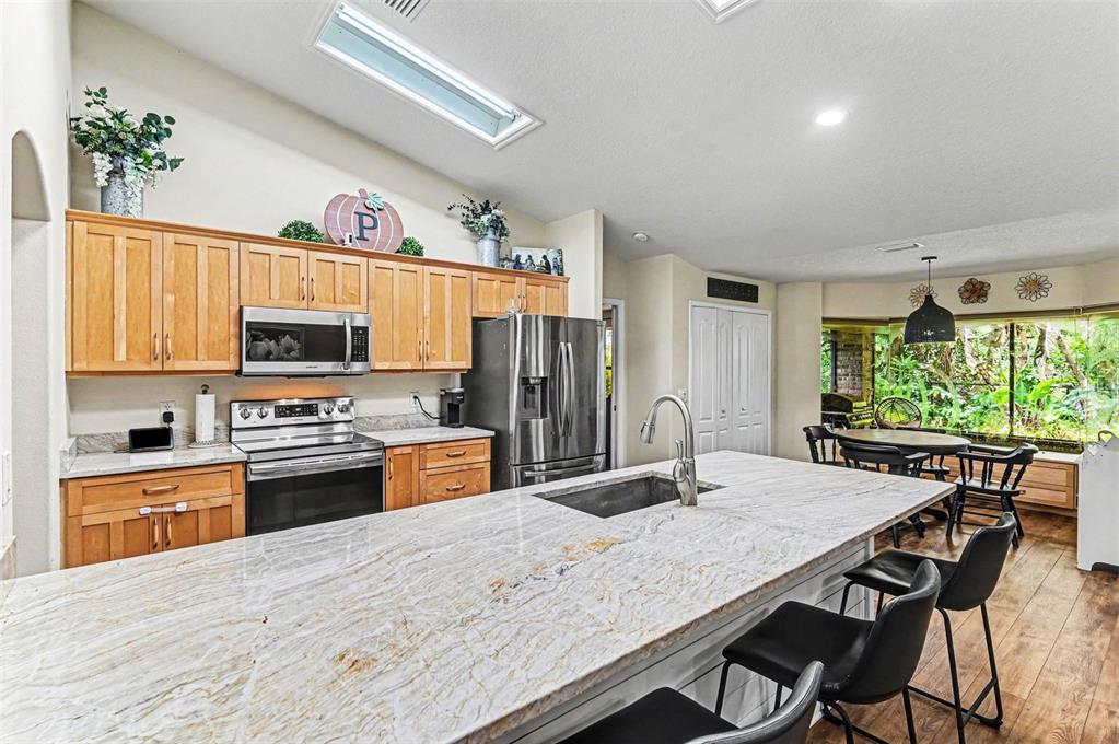 A kitchen features light wood cabinets, a large granite island, and a dining nook — 6040 SPRUCE POINT CIRCLE, PORT ORANGE, FL