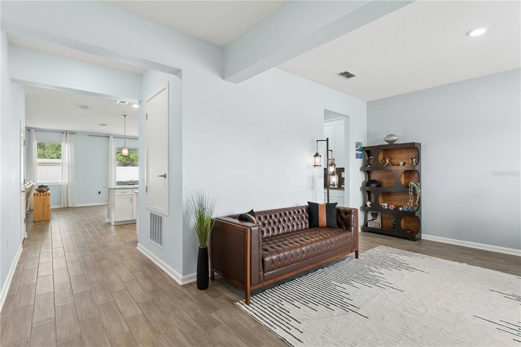 A living area features a brown leather tufted sofa, a bookshelf, and light wood-look flooring — 1855 BLACK MAPLE PLACE, OCOEE, FL