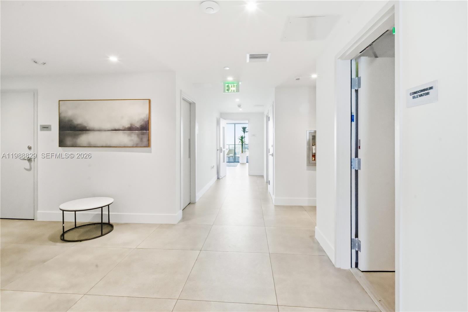 A bright, minimalist hallway features white walls, tiled floors, an elevator, and an exit sign — 239 SW 9th St # 2401, Miami FL 33130, MIAMI, FL