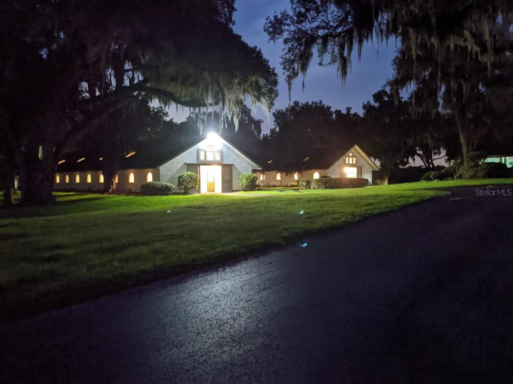 A white building with a gabled roof is illuminated at night amidst trees and grass — 5540 SE 157TH STREET ROAD, SUMMERFIELD, FL