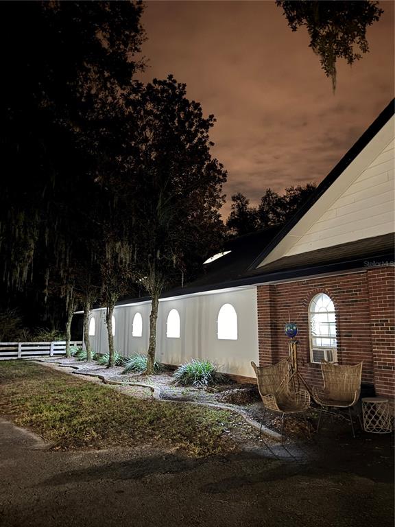A brick and white exterior wall features arched windows and two wicker chairs at night — 5540 SE 157TH STREET ROAD, SUMMERFIELD, FL