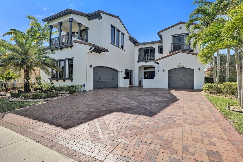 A two-story house with a brick driveway, two garages, and balconies under a blue sky — 10292 Emerson St, Parkland FL 33076, PARKLAND, FL