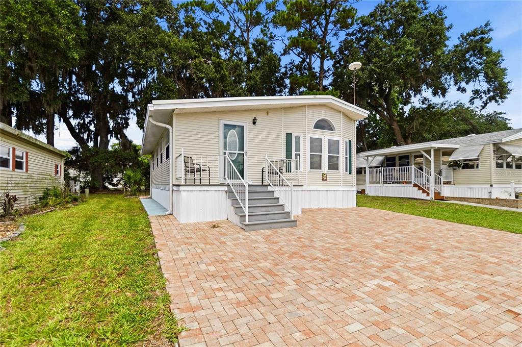 A beige manufactured home features a brick paver driveway and a small front porch — 67 CITRUS RIDGE DRIVE, DAVENPORT, FL