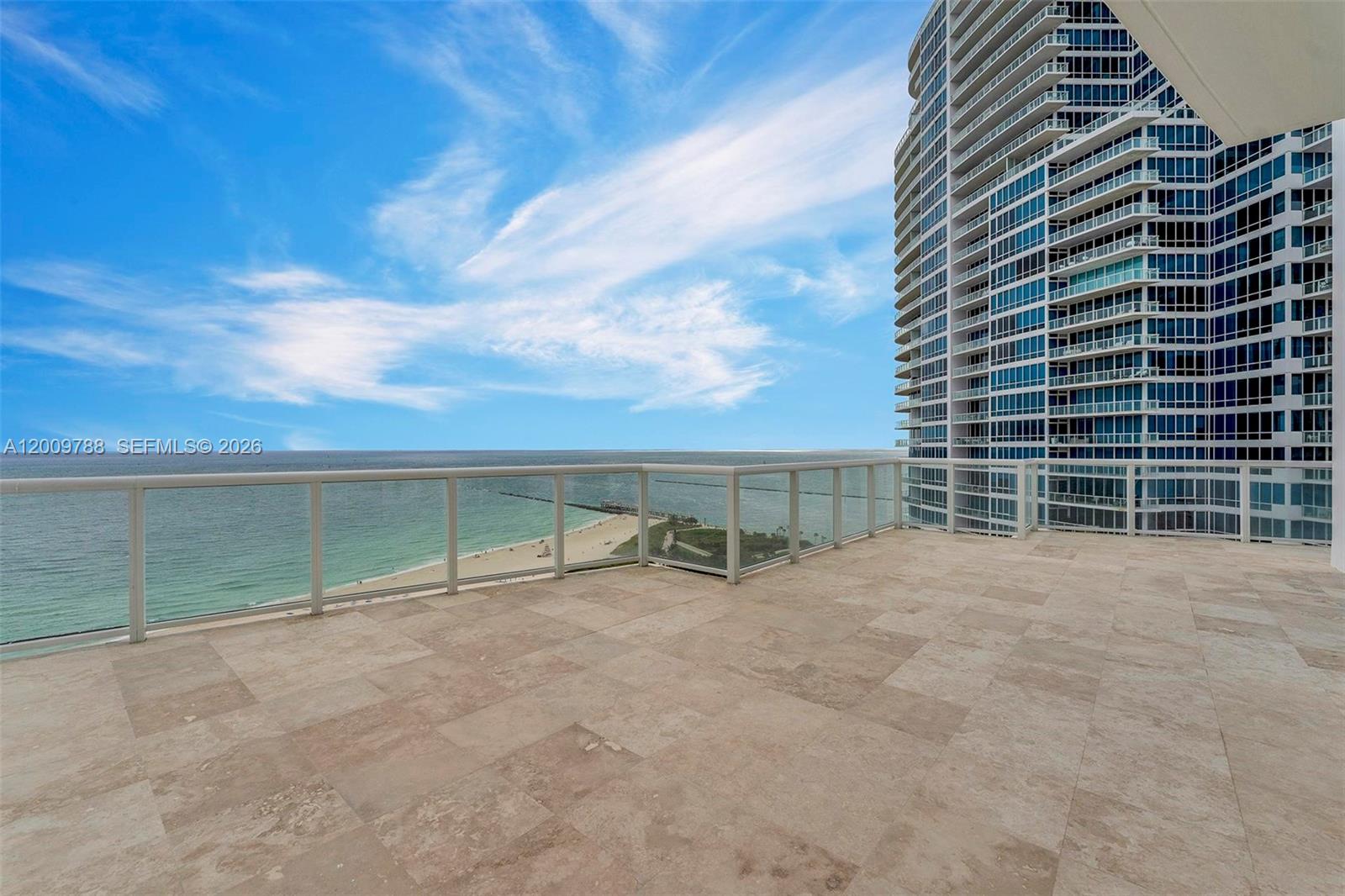 A spacious balcony with stone tile flooring overlooks the ocean and a nearby high-rise building — 50 S Pointe Dr # 2102, Miami Beach FL 33139, MIAMI BEACH, FL