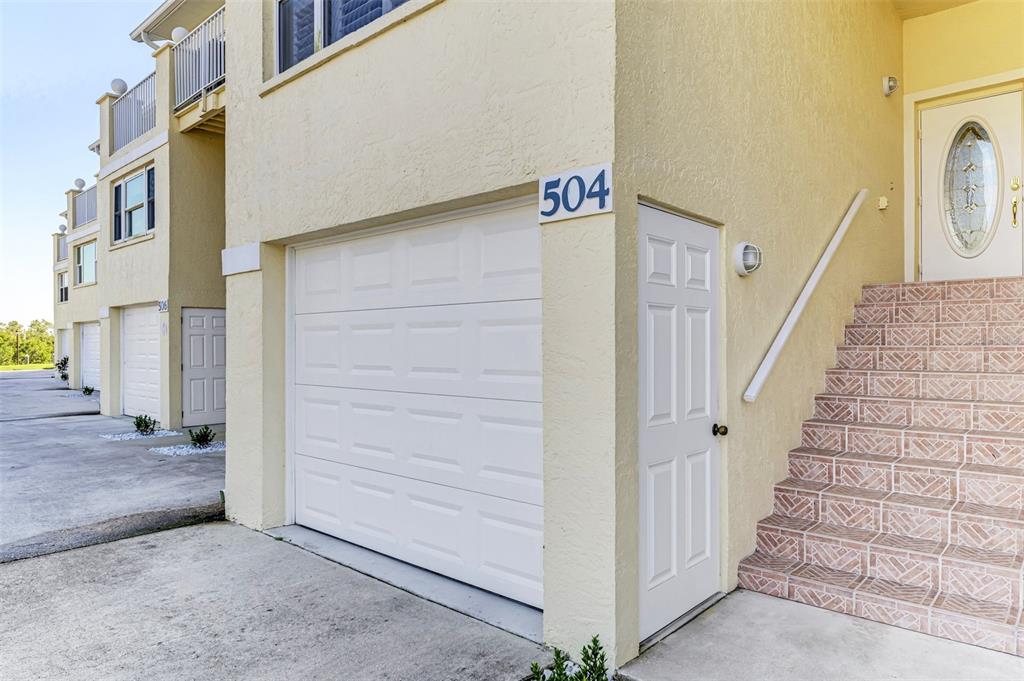 A yellow multi-story townhouse exterior features a white garage door, a side door, and stairs — 4410 WARREN AVENUE UNIT 504, PORT CHARLOTTE, FL