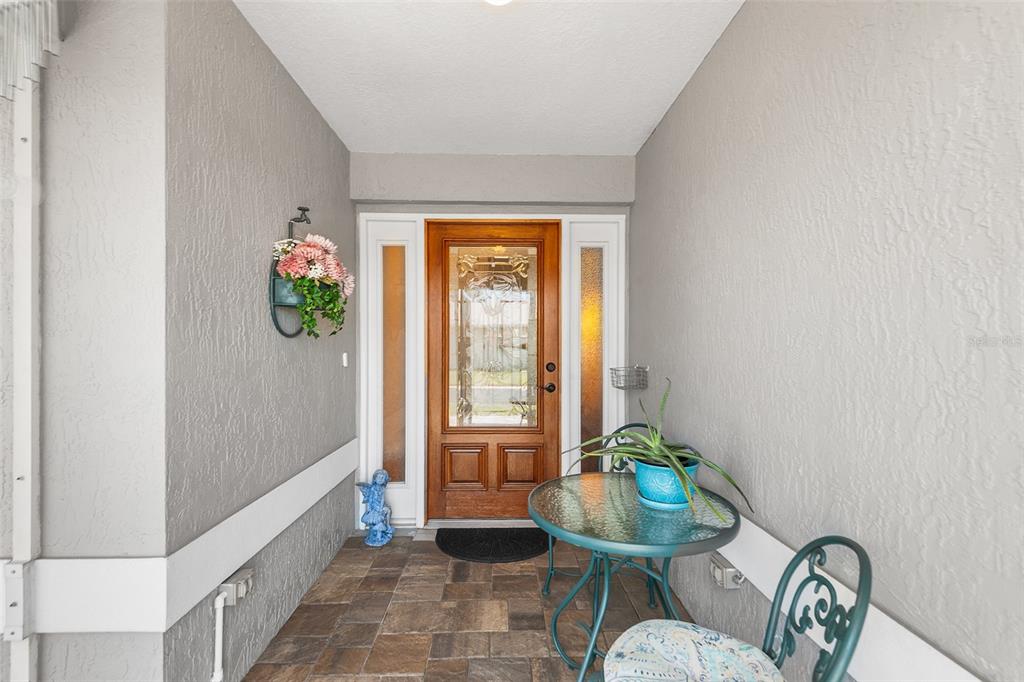 A covered entryway features a wooden front door with glass panels, tile flooring, and furniture — 510 EASTLAKE DR, HAINES CITY, FL