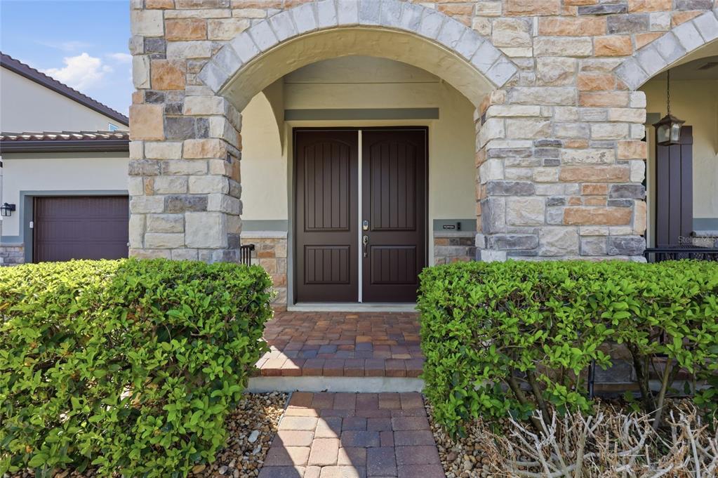 A stone-faced house exterior features a covered entryway with double doors and a brick walkway — 1646 HOLCOMB CREEK STREET, WINTER GARDEN, FL