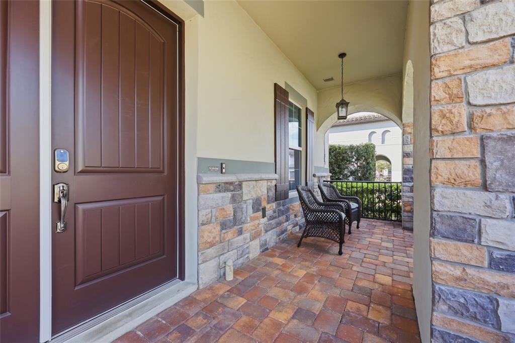 A covered front porch features stone veneer walls, brick pavers, and two wicker chairs — 1646 HOLCOMB CREEK STREET, WINTER GARDEN, FL