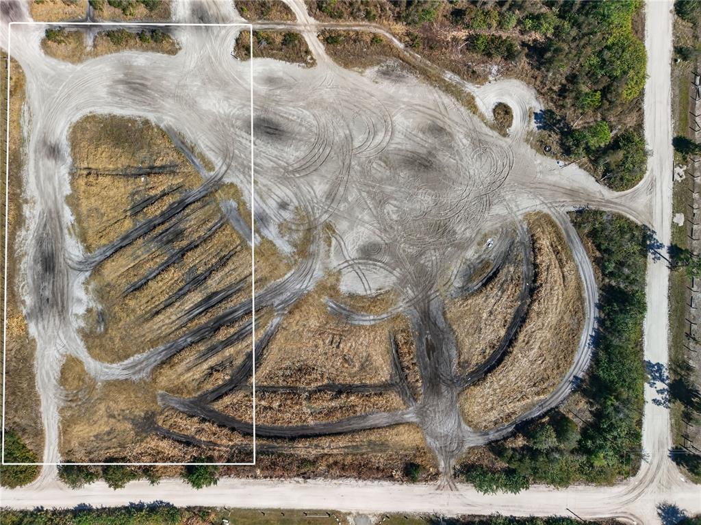 An aerial view shows a large, cleared dirt lot with tire tracks and surrounding vegetation — 7492 SWISS BOULEVARD, PUNTA GORDA, FL