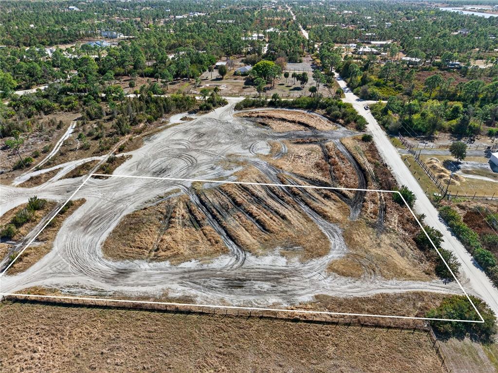An aerial view shows a cleared, rectangular plot of land with tire tracks and fencing — 7492 SWISS BOULEVARD, PUNTA GORDA, FL