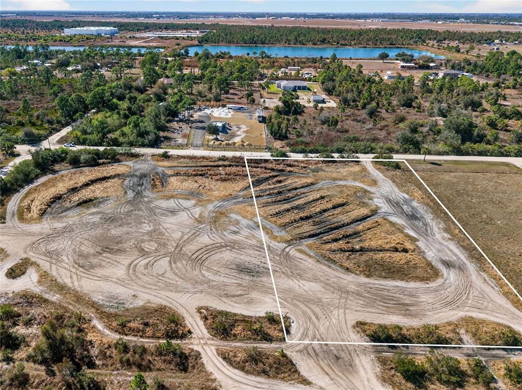 An aerial view shows a large, cleared dirt lot with tire tracks and outlined boundaries — 7492 SWISS BOULEVARD, PUNTA GORDA, FL