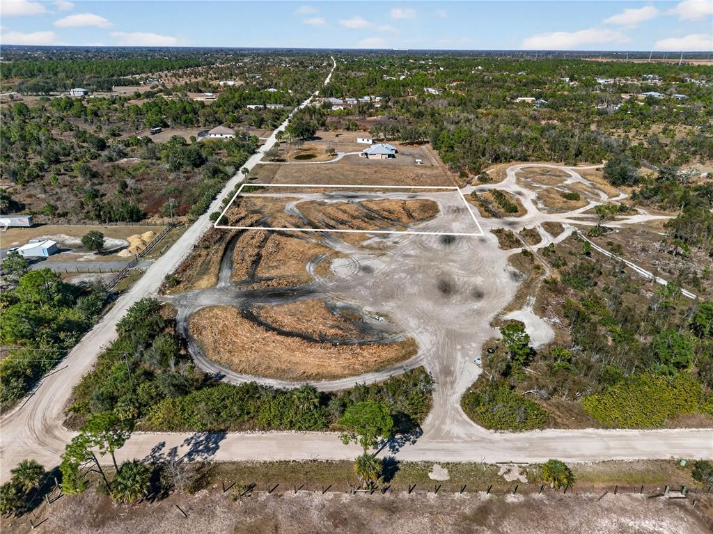 An aerial view shows a large, cleared dirt lot outlined in white within a rural landscape — 7492 SWISS BOULEVARD, PUNTA GORDA, FL
