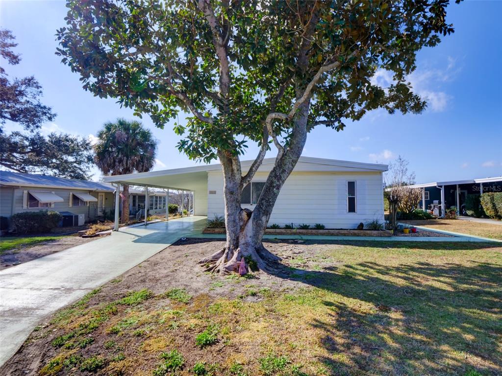 A single-story mobile home with a carport and a large tree in the front yard — 2218 ORANGEWOOD CIRCLE UNIT 1540, ZELLWOOD, FL