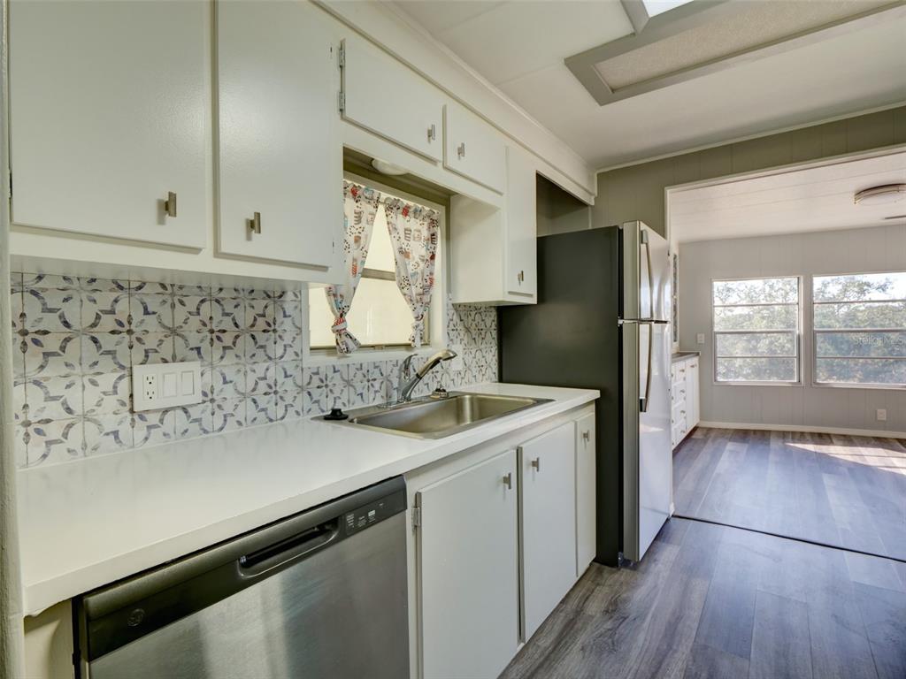 A kitchen features white cabinets, a patterned tile backsplash, stainless steel appliances, and wood-look flooring — 2218 ORANGEWOOD CIRCLE UNIT 1540, ZELLWOOD, FL